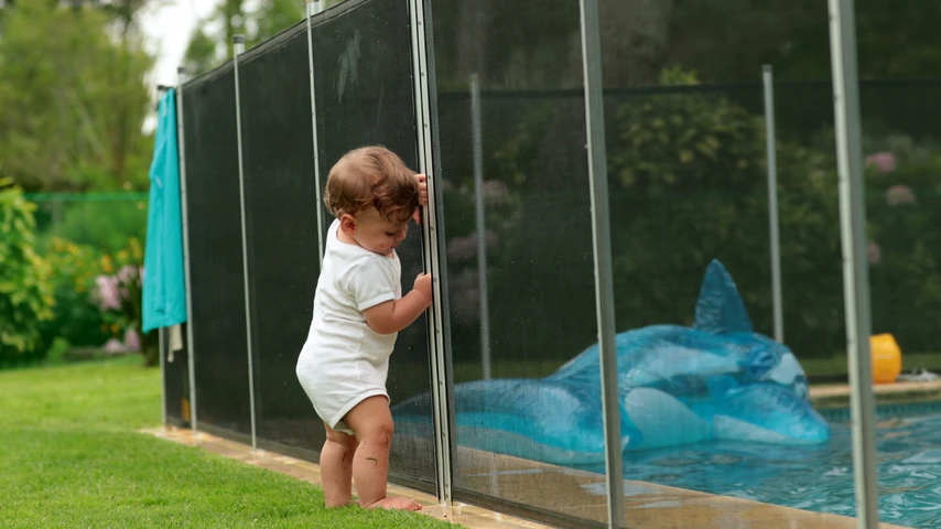 Baby leaning on swimming pool fence protection. Infant standing on safety gate